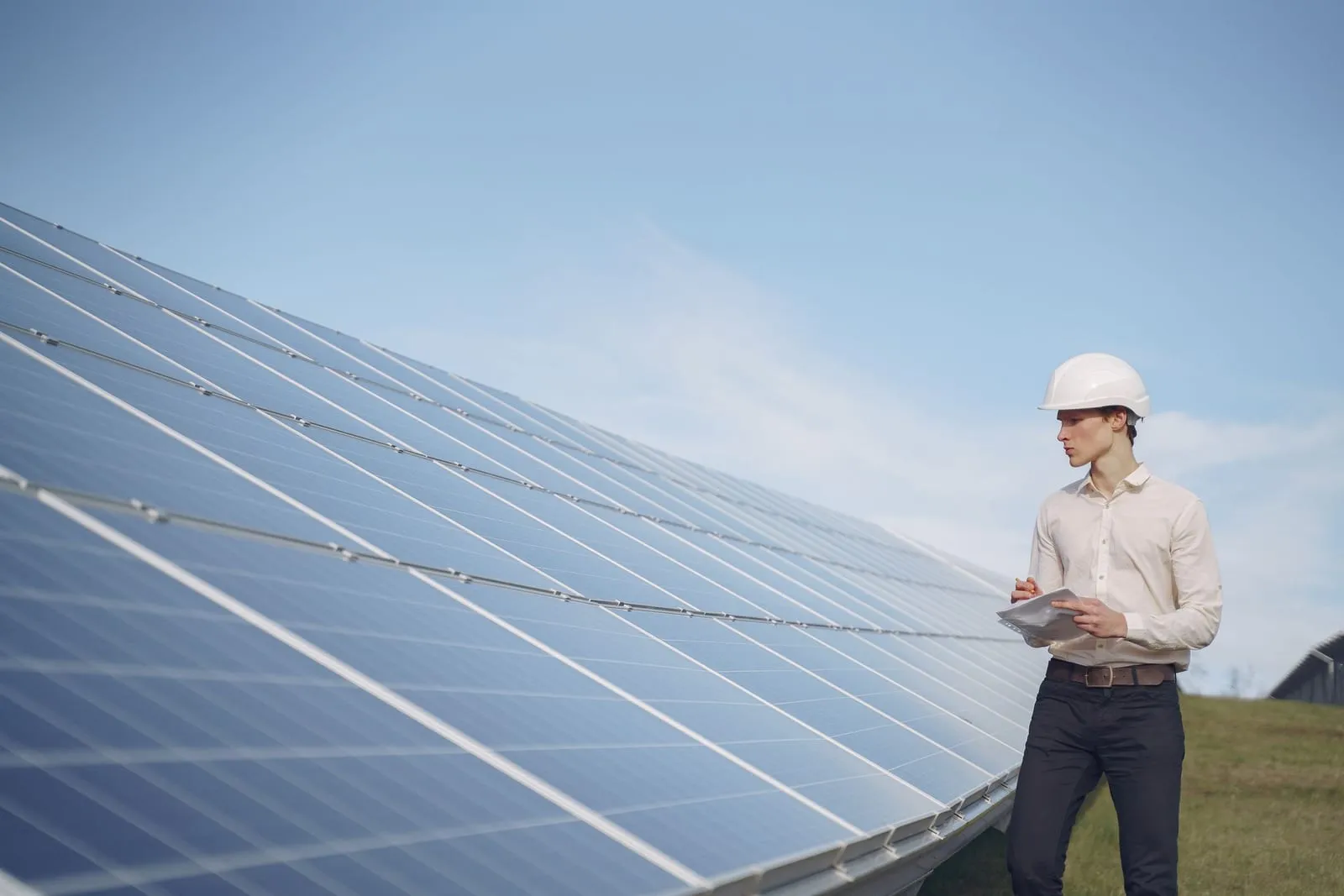 Engineer in a white hard hat inspecting a solar panel array